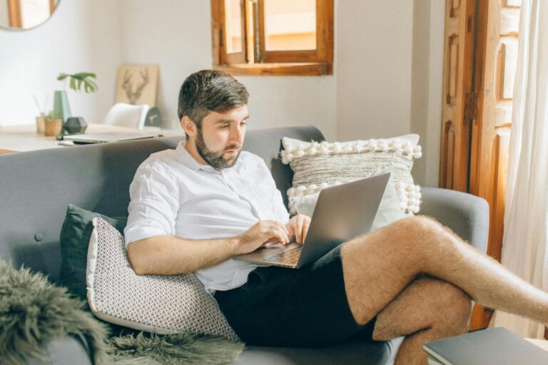 Adult man sitting on couch using laptop working remotely from home
