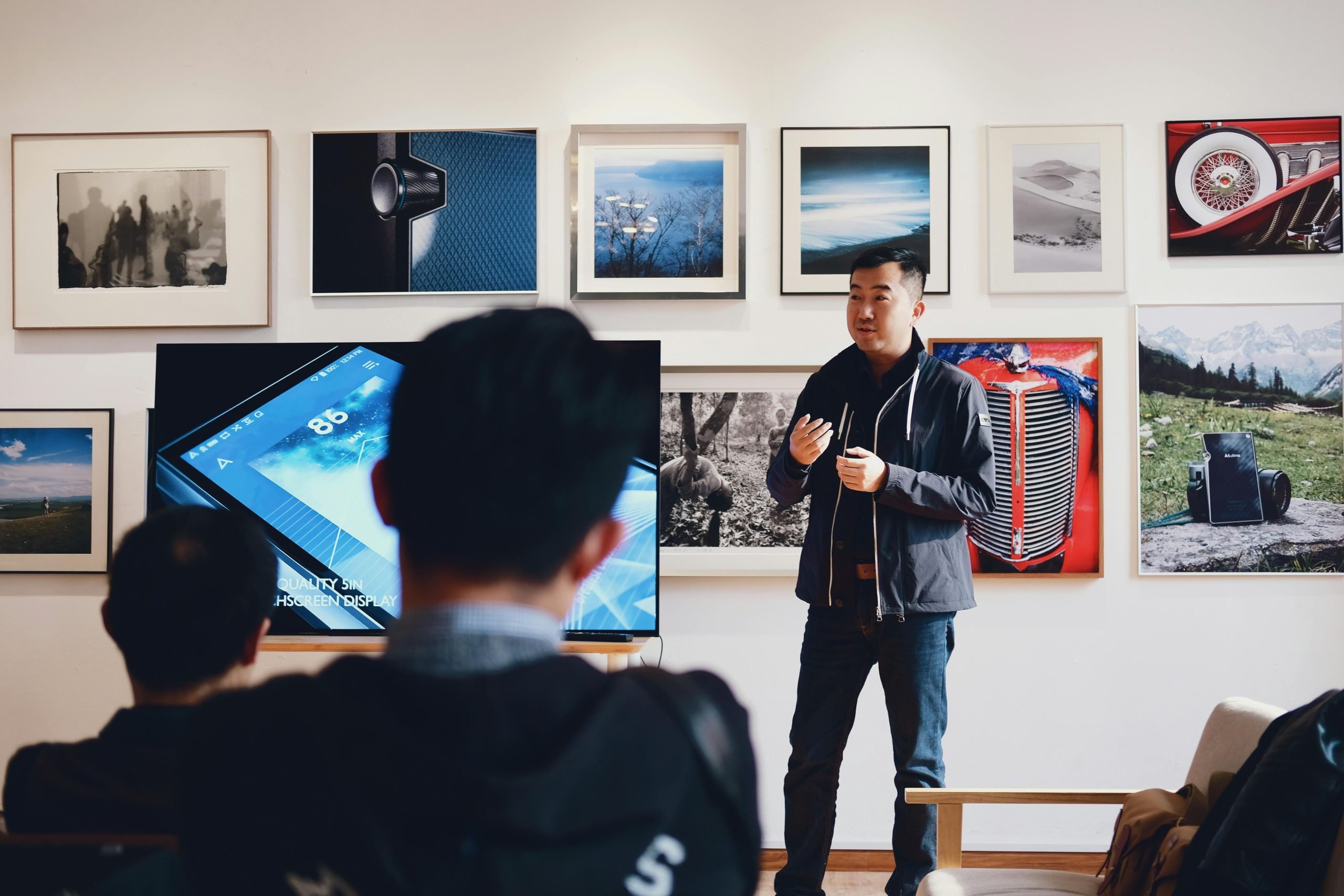 Young man presenting to small audience with photography gallery wall backdrop