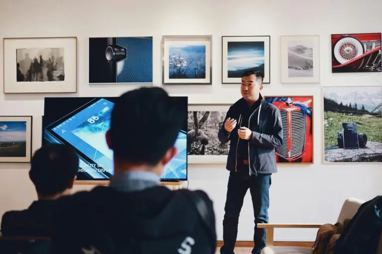Young man presenting to small audience with photography gallery wall backdrop