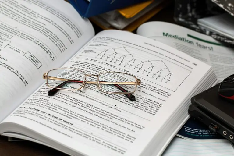Open book with reading glasses surrounded by study materials and laptop