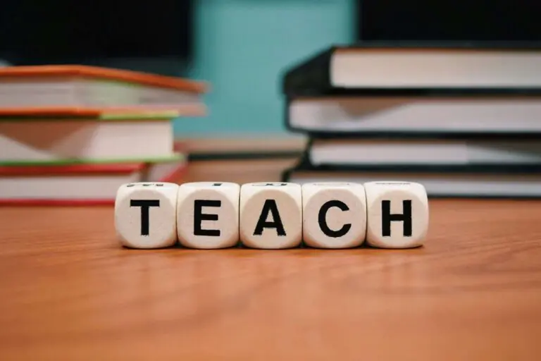 Wooden dice spelling TEACH on desk with stacked books blurred background