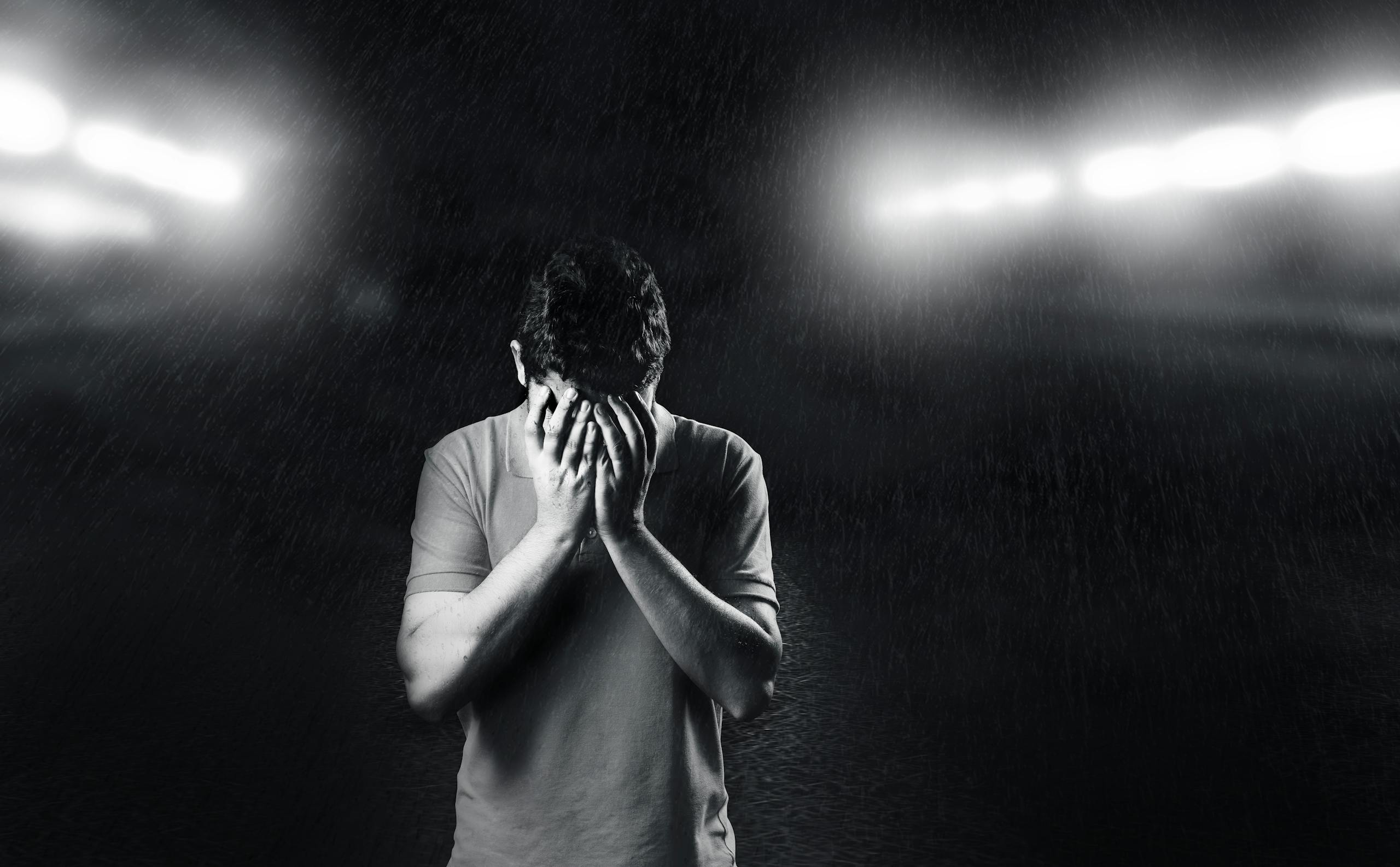 Black and white photo of man covering face expressing emotion and solitude