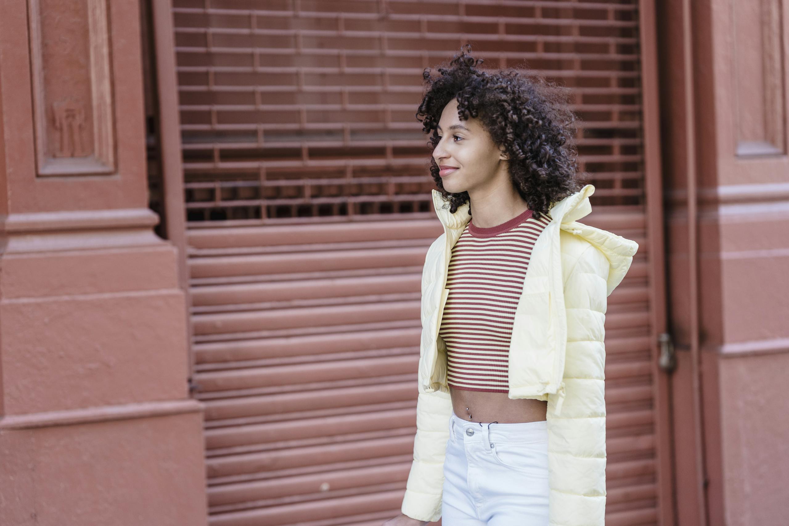 Charming young woman with curly hair enjoying walk in city urban setting