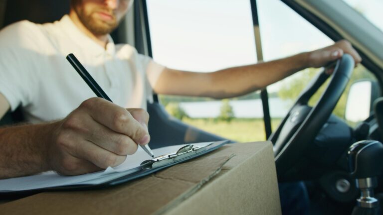 Close-up of delivery driver inside van writing on clipboard for logistics work