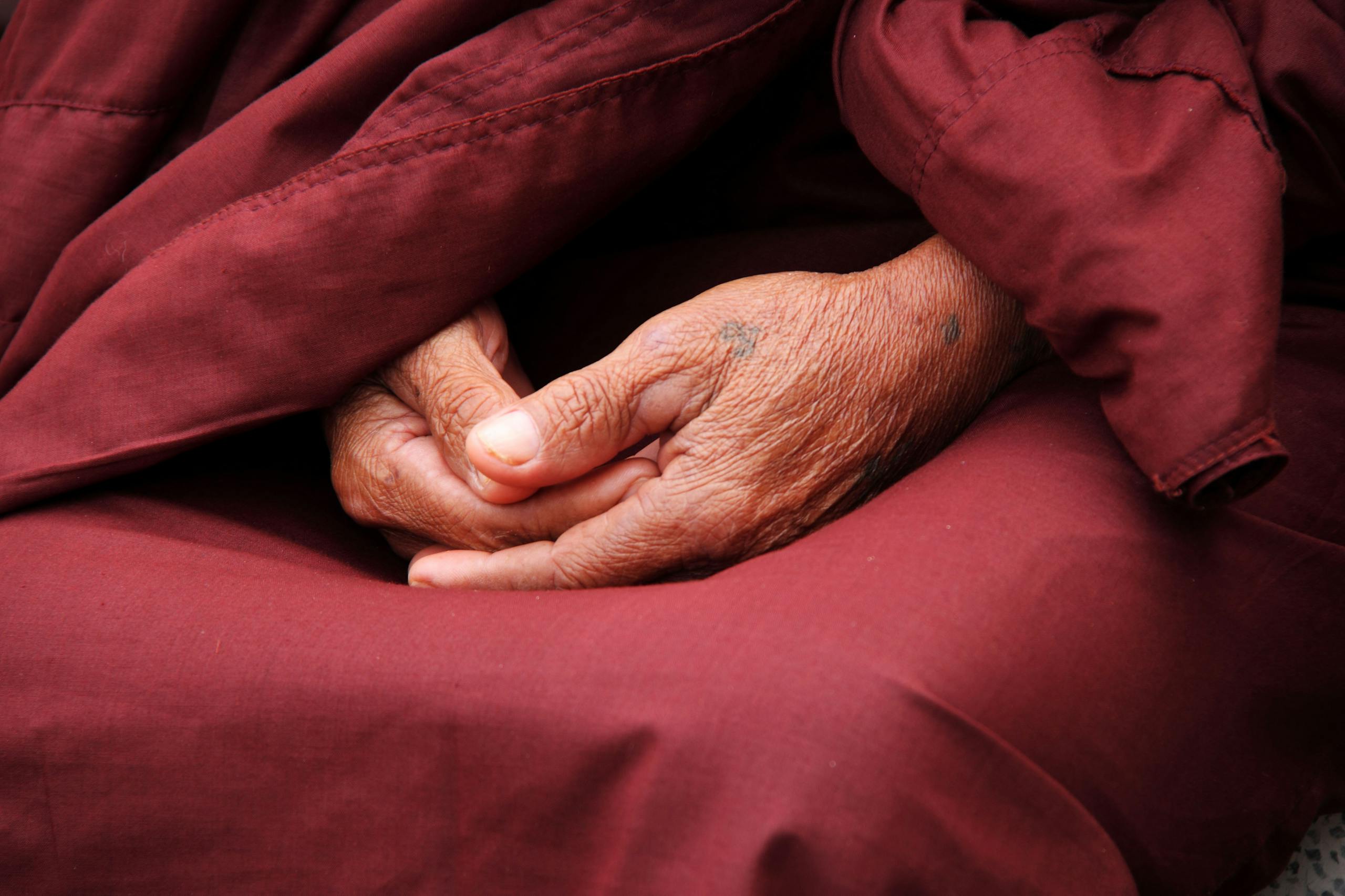 Close-up of monk's hands in prayer wrapped in maroon robe symbolizing spirituality