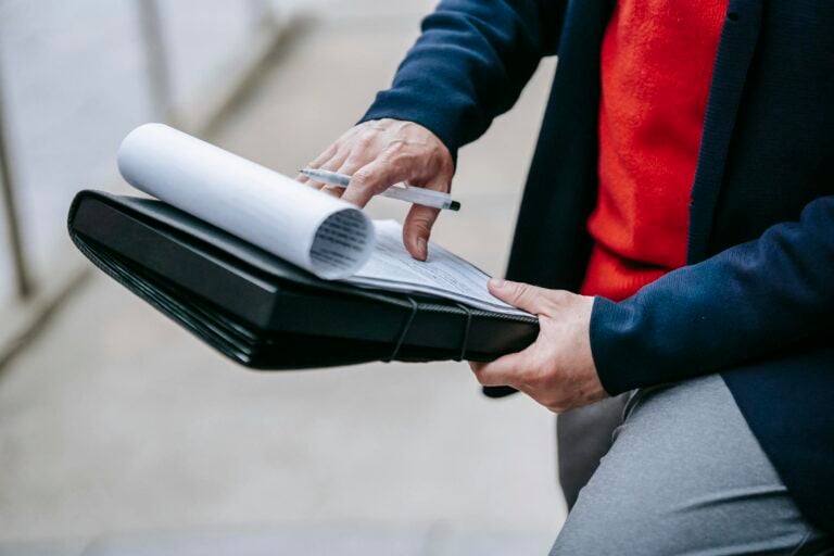 Close-up of professional person reviewing documents outdoors with focus on writing materials