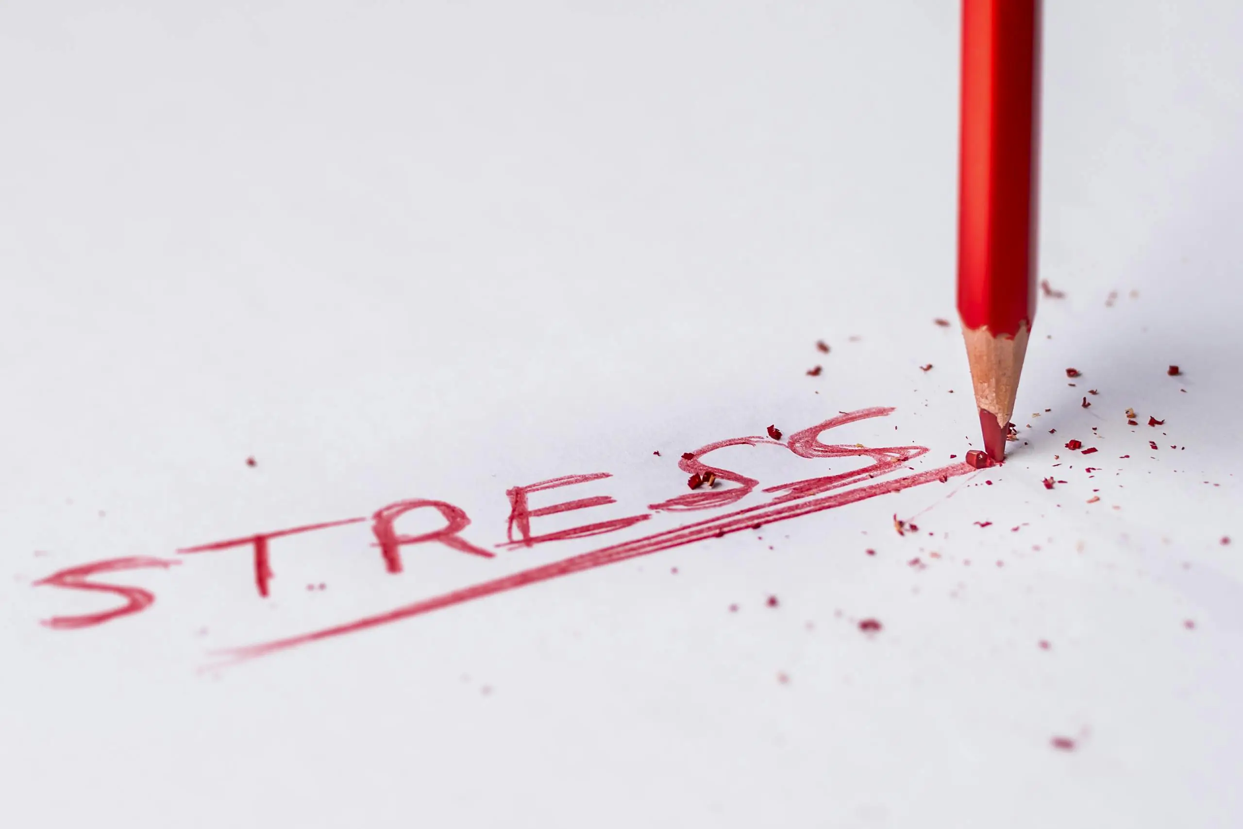 Close-up of red pencil writing stress on paper symbolizing pressure.