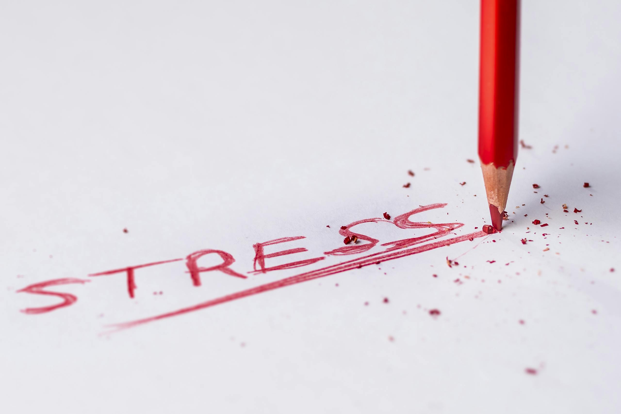 Close-up of red pencil writing stress on paper symbolizing pressure.