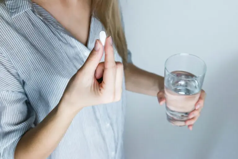 Close-up of woman holding pill and glass of water ready to take medication