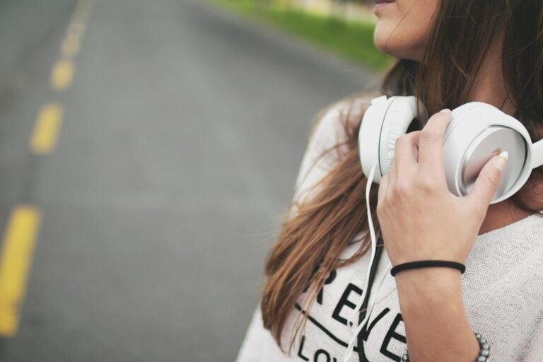 Woman outdoors on quiet road holding headphones while enjoying music.