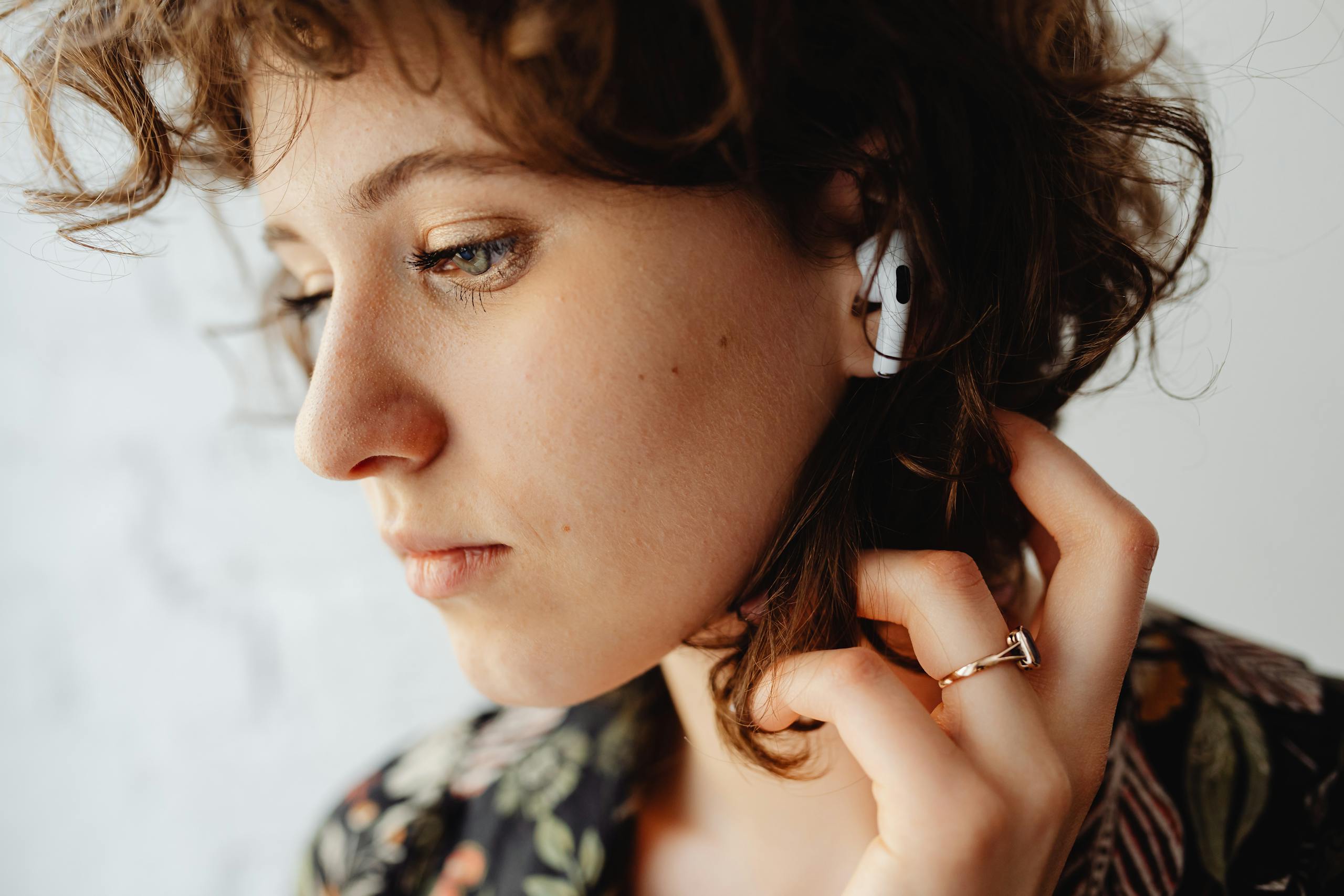 Woman with curly hair listening to music using wireless earbuds.