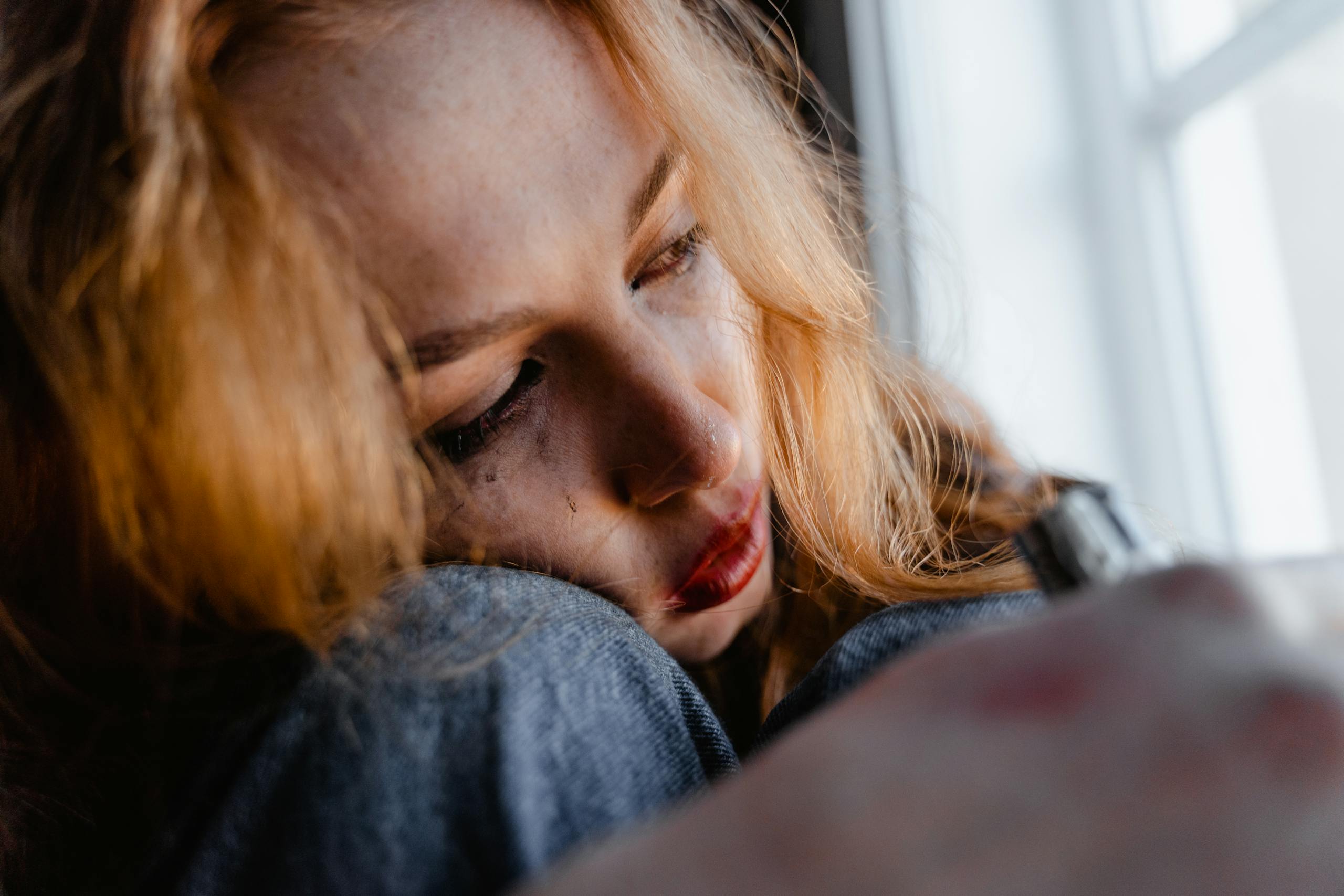 Close-up of woman with red hair in thoughtful, emotional moment indoors.