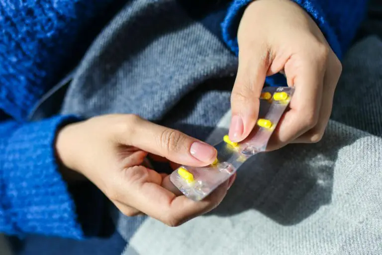 Close up of woman's hands holding yellow pill blister pack indoors