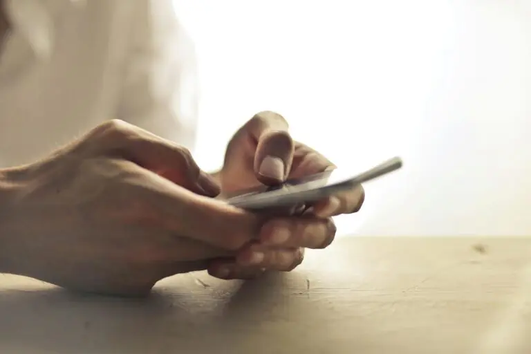 Close-up of hands holding smartphone on table indoors.