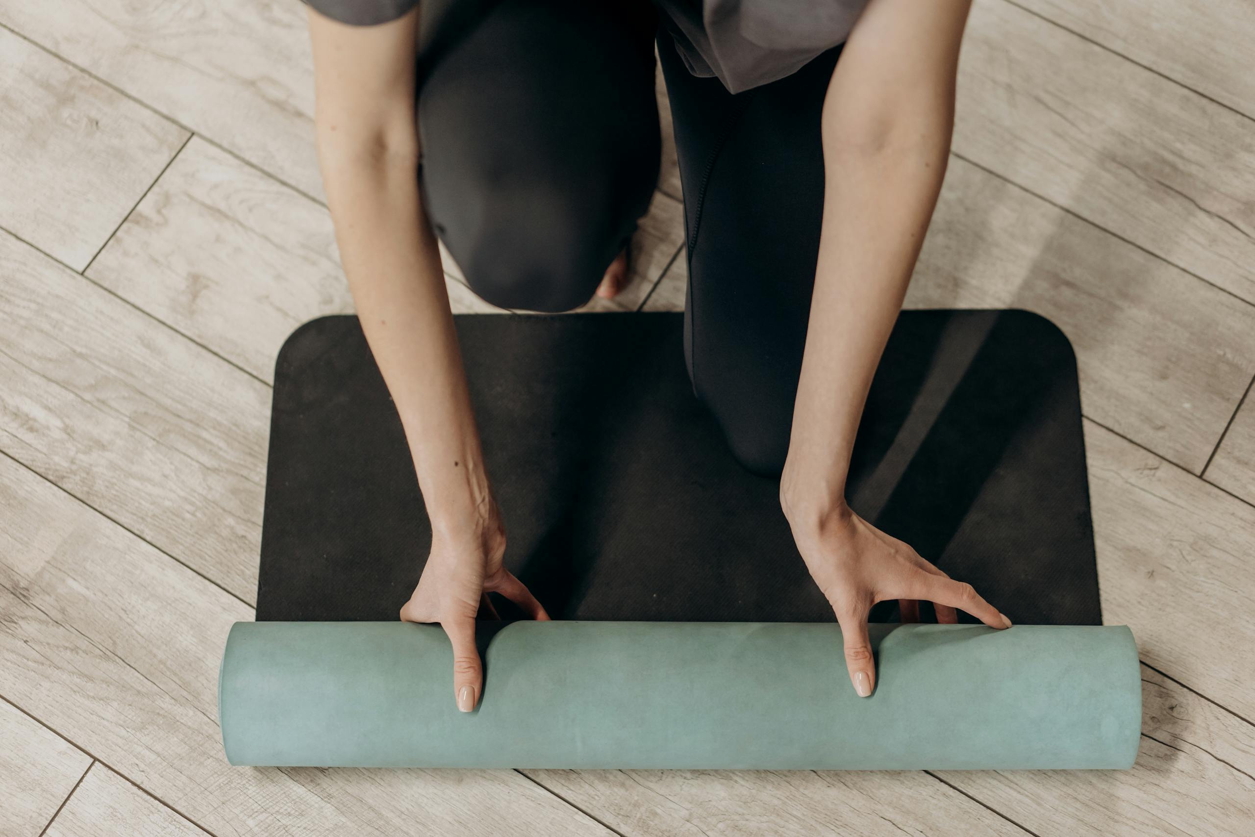 Close up of individual rolling out a yoga mat on wooden floor ready for home workout