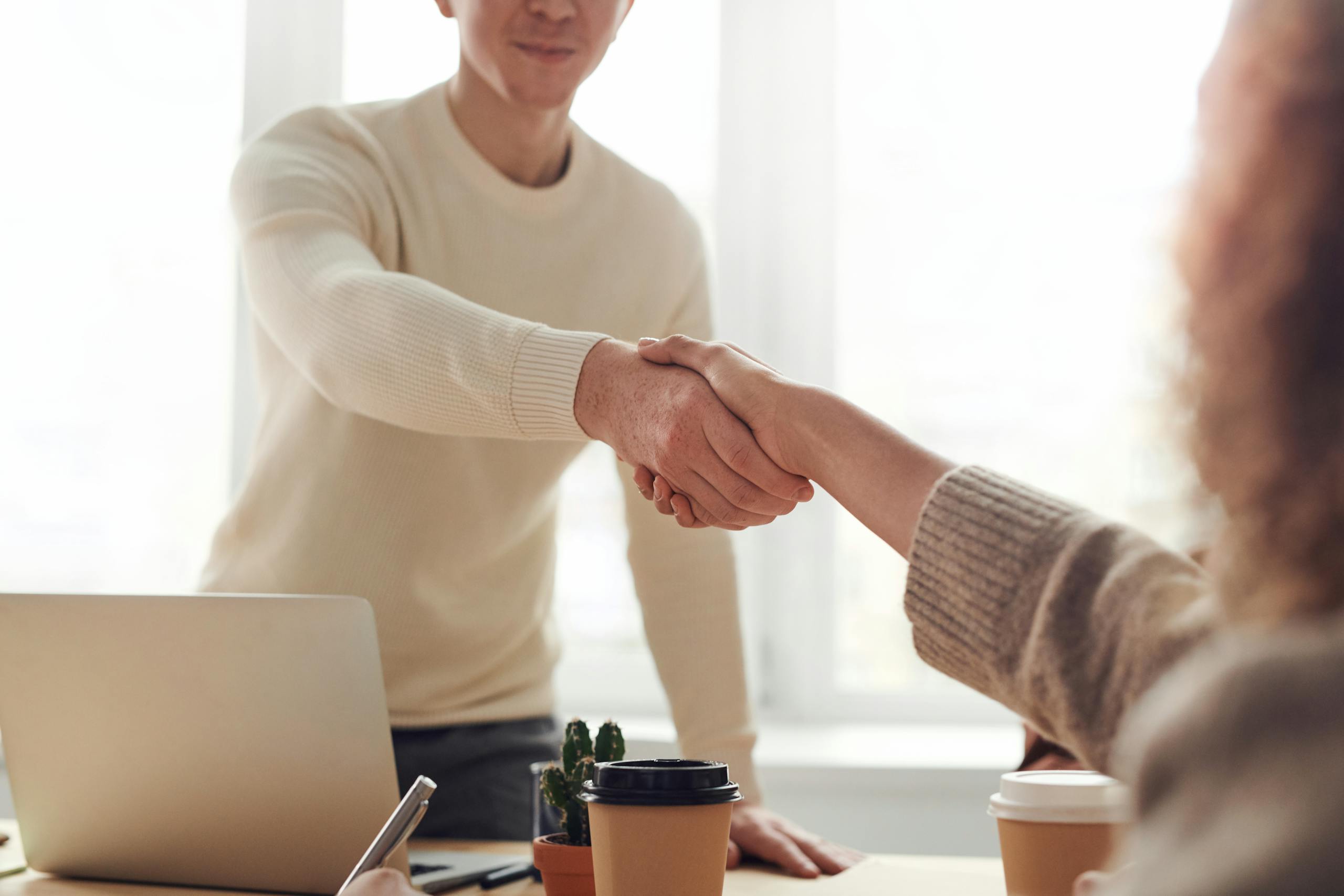 Close up of professionals shaking hands over coffee in modern office.