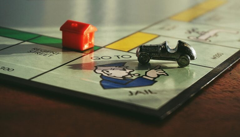 Close-up of Monopoly board game with toy car and red house near jail.