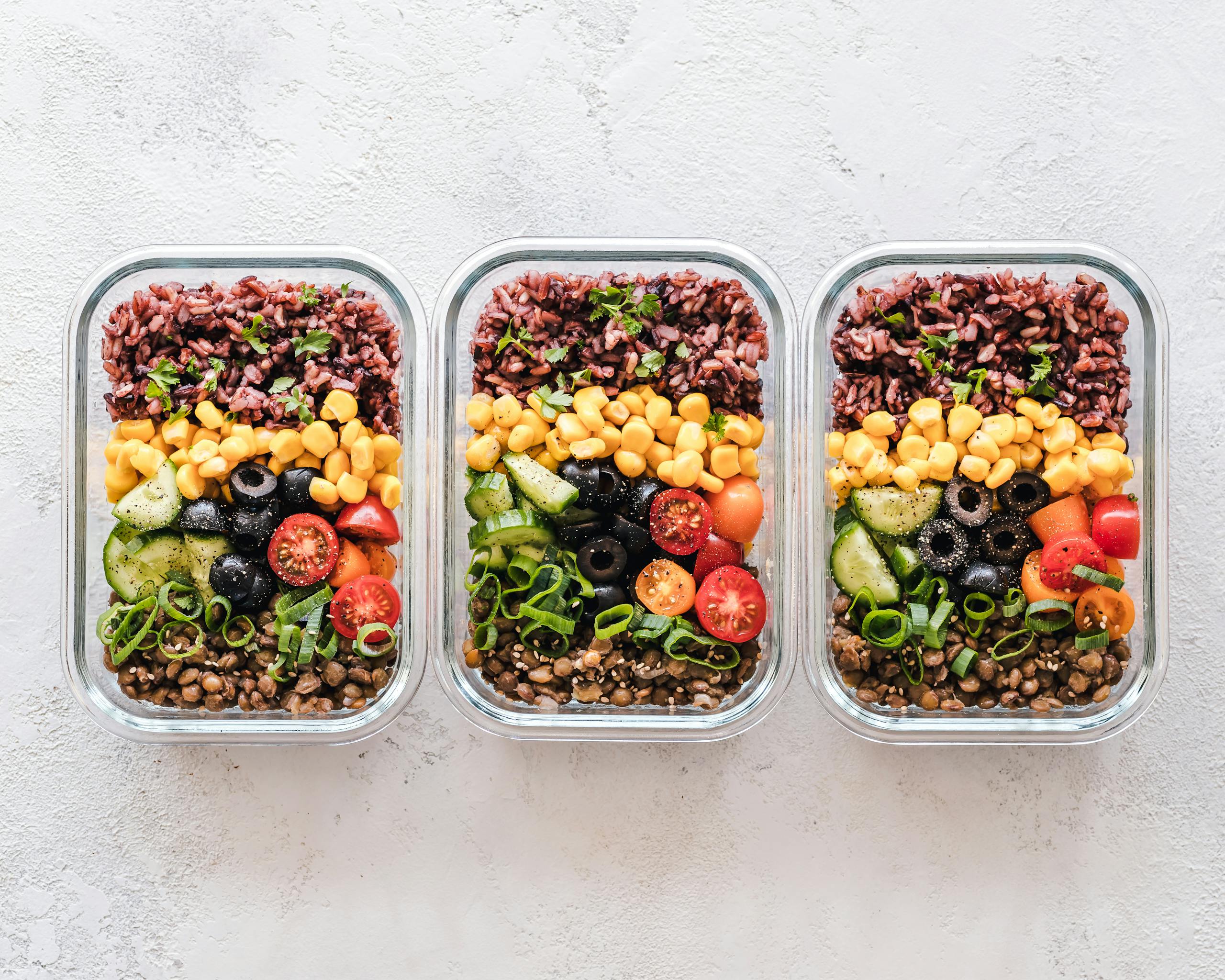 Colorful healthy meal prep with corn olives tomatoes and lentils in glass containers