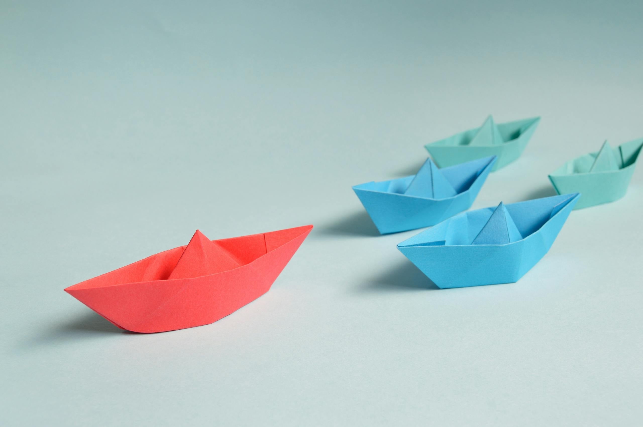 Colorful origami boats arranged depicting leadership and teamwork symbolism