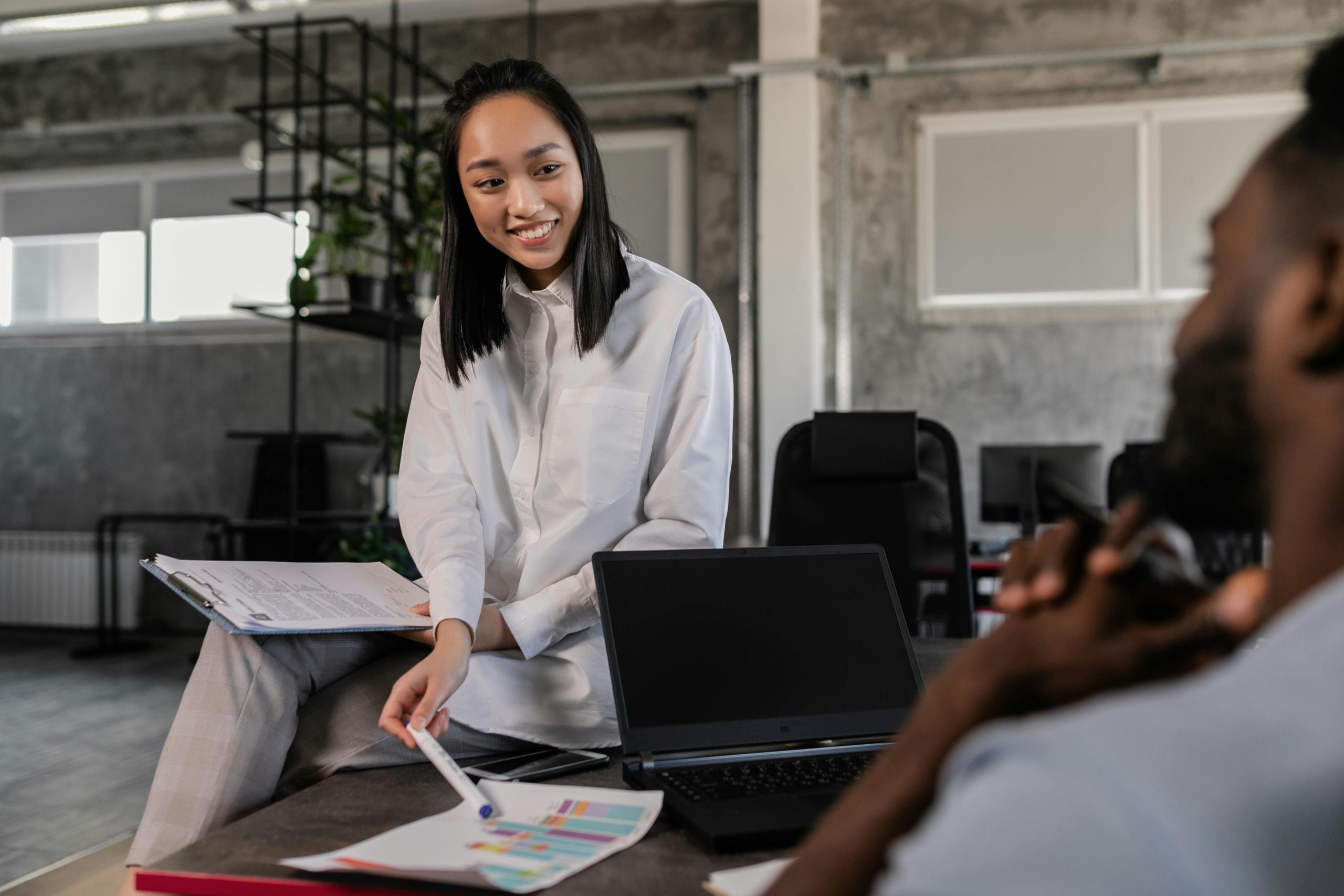 Young professional woman smiling while presenting data to colleague in modern office