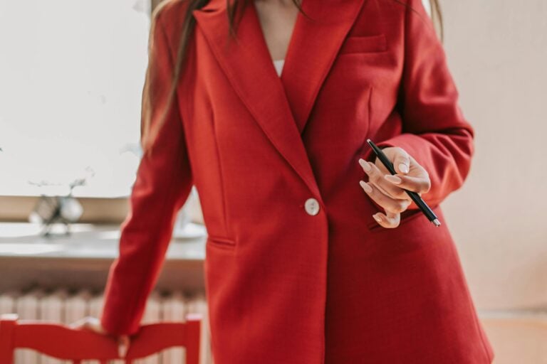Confident woman in red blazer holding pen ready for business leadership role.