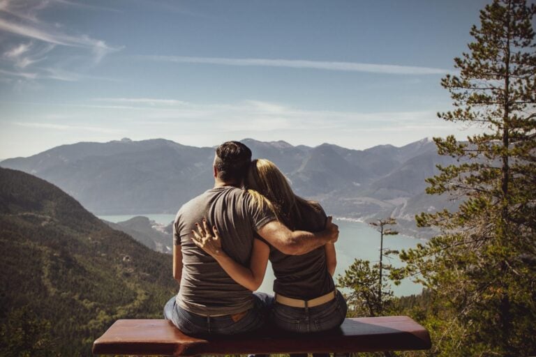 Couple sitting on bench embracing scenic mountain view embodying romantic nature escape
