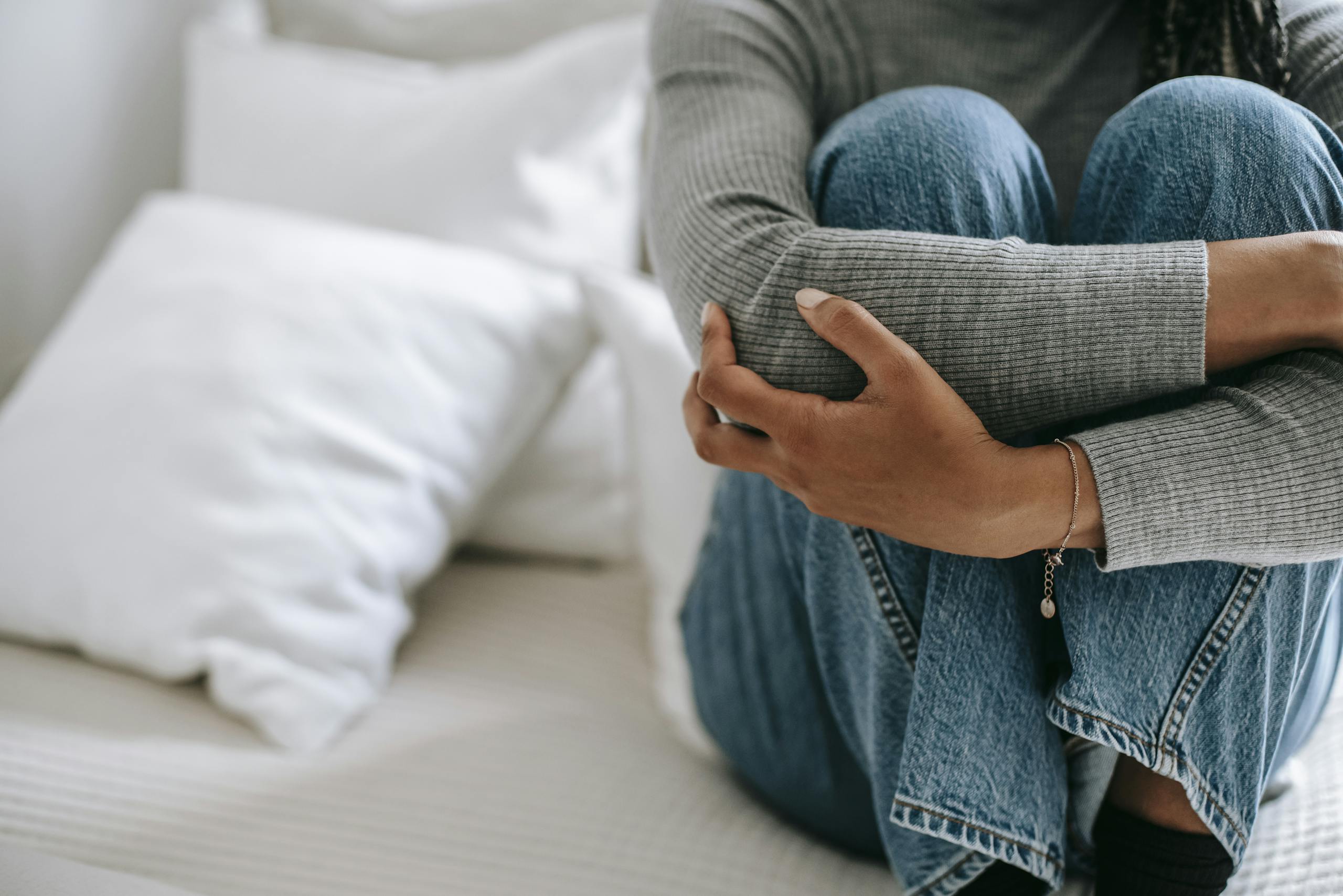 Faceless woman feeling helpless and frustrated with knees to chest on bed.