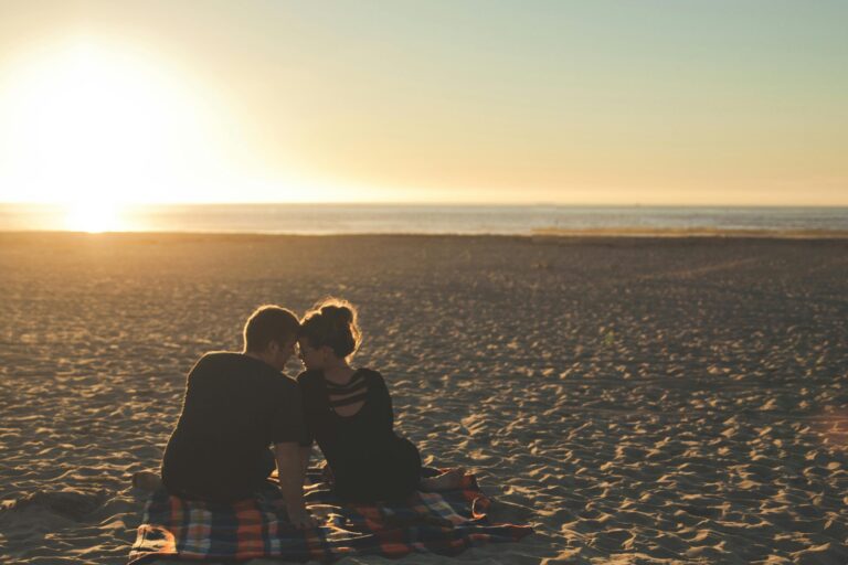 Two people sitting close together on beach at sunset, intimate moment