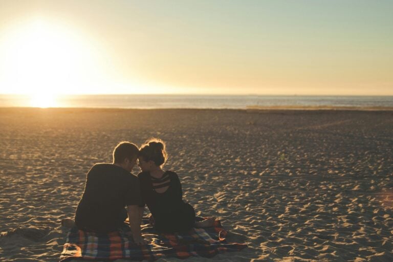 Two people sitting close together on beach at sunset, intimate moment