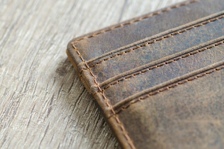 Close-up of brown leather wallet on textured wooden surface with visible stitching.