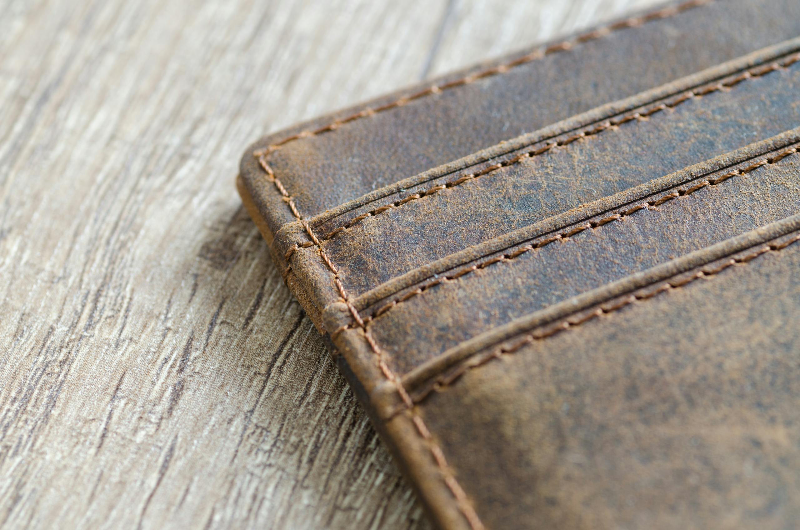 Close-up of brown leather wallet on textured wooden surface with visible stitching.