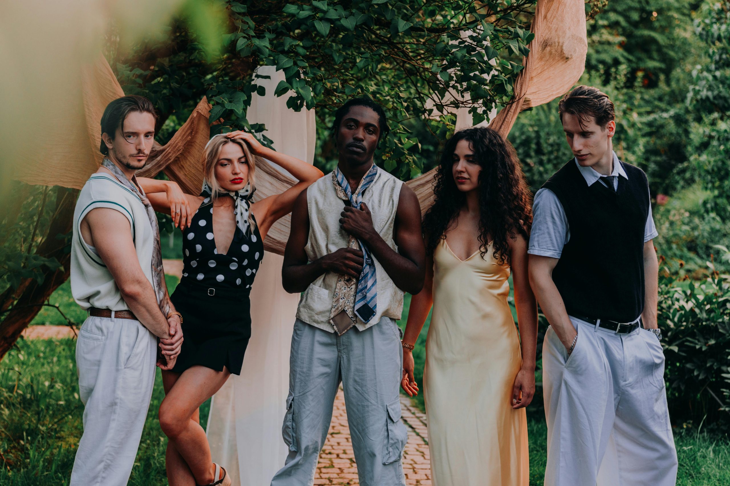 Five diverse young adults posing together in a lush garden setting with natural warmth