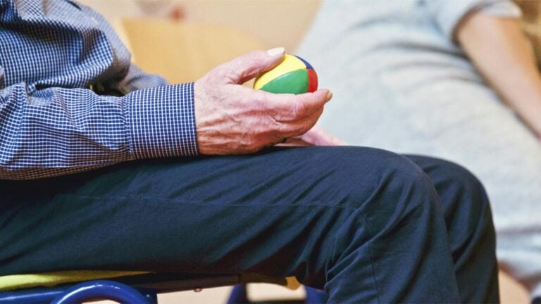 Elderly man holding colorful therapy ball indoors promoting relaxation.