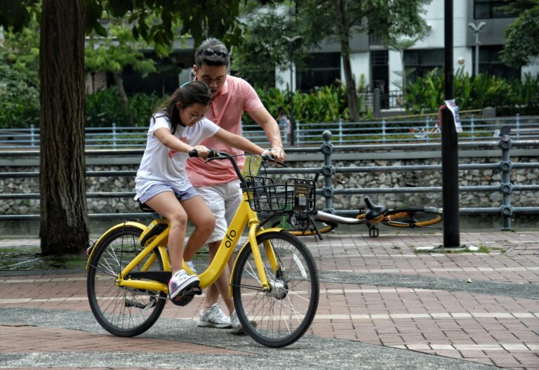 Father teaches daughter to ride yellow bicycle in singapore park bonding moment