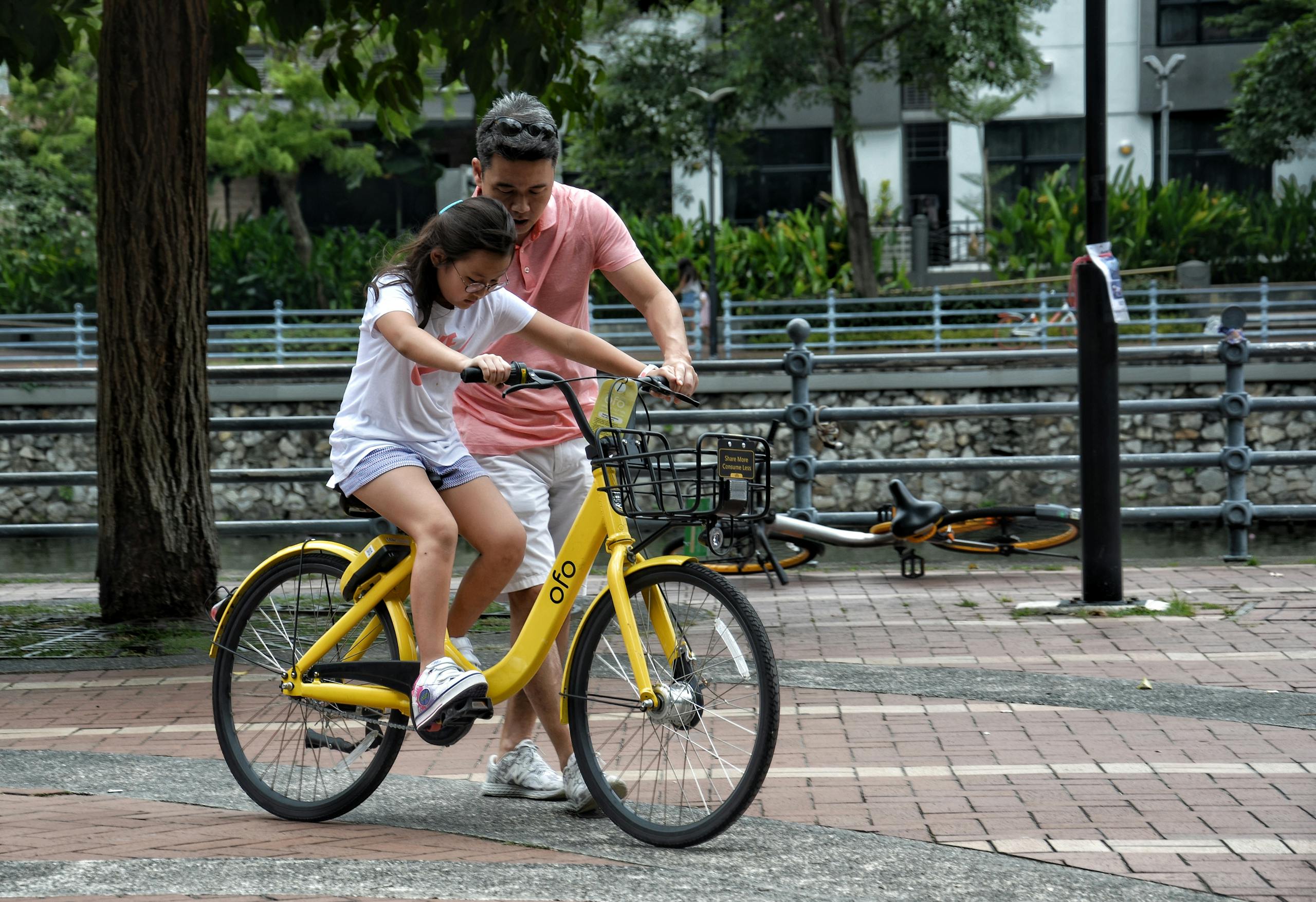 Father teaches daughter to ride yellow bicycle in singapore park bonding moment