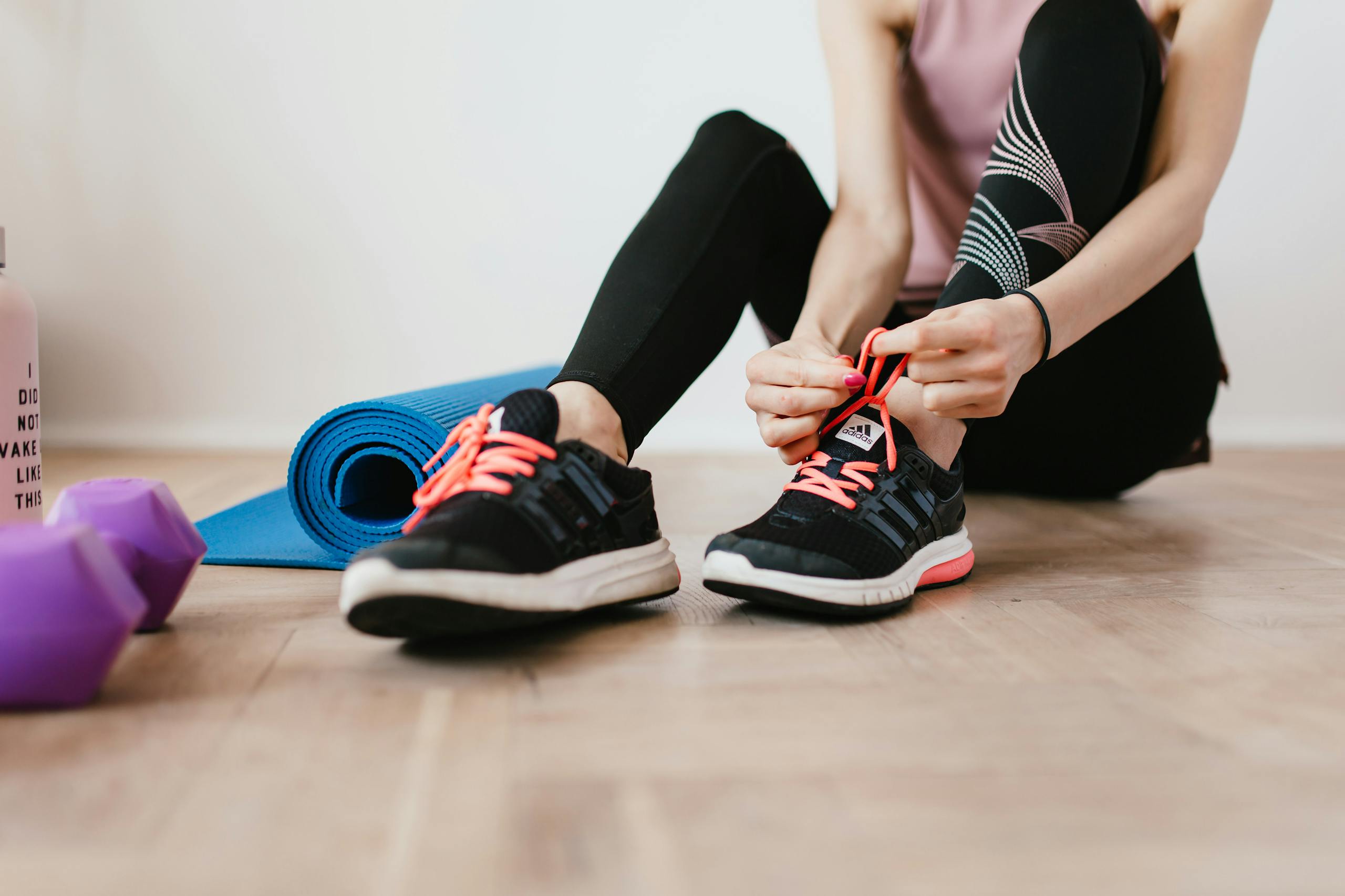 Woman tying shoelaces before indoor workout with yoga mat and dumbbells.