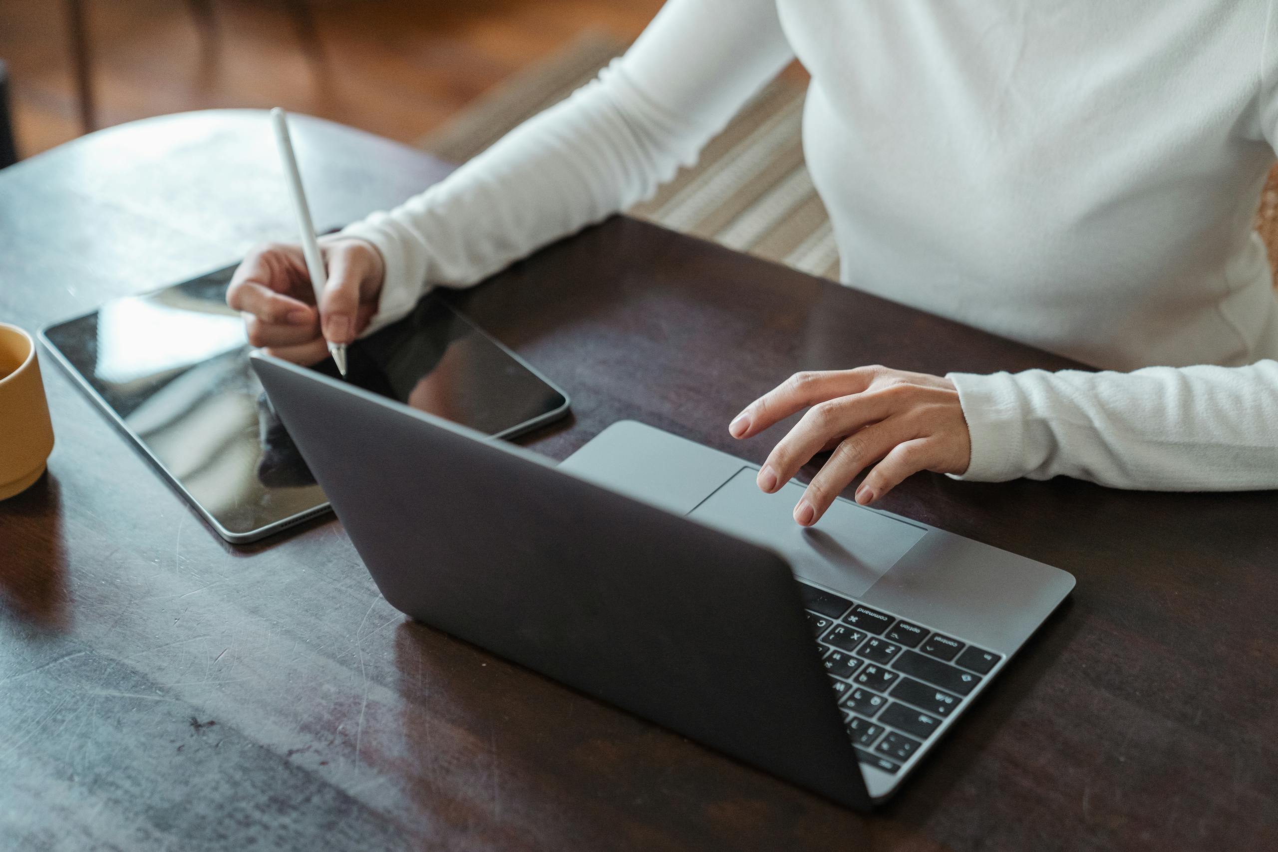 Businesswoman multitasking with laptop and tablet in modern office environment.