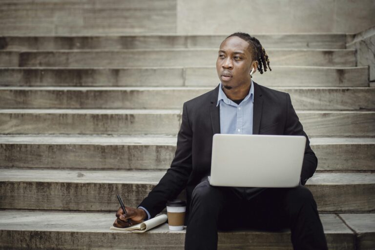 Young professional focused on laptop work while sitting on outdoor steps.
