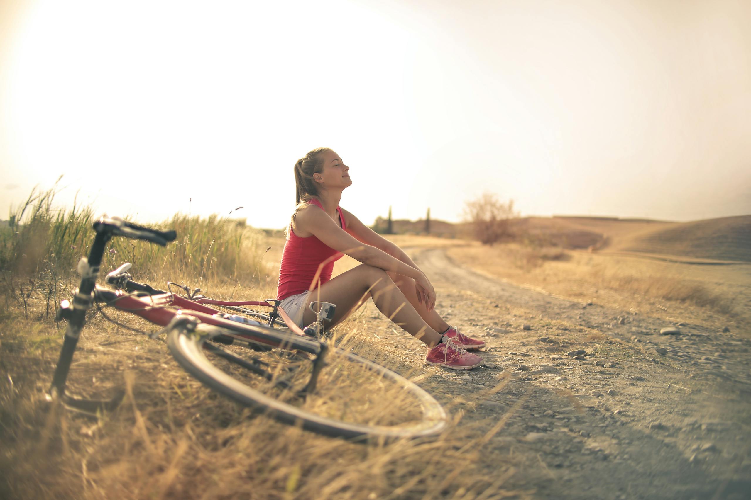 Woman sitting roadside in rural field with bicycle enjoying nature peacefully
