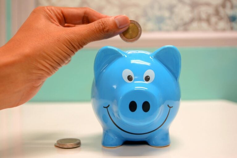Hand inserting coin into blue piggy bank for savings.
