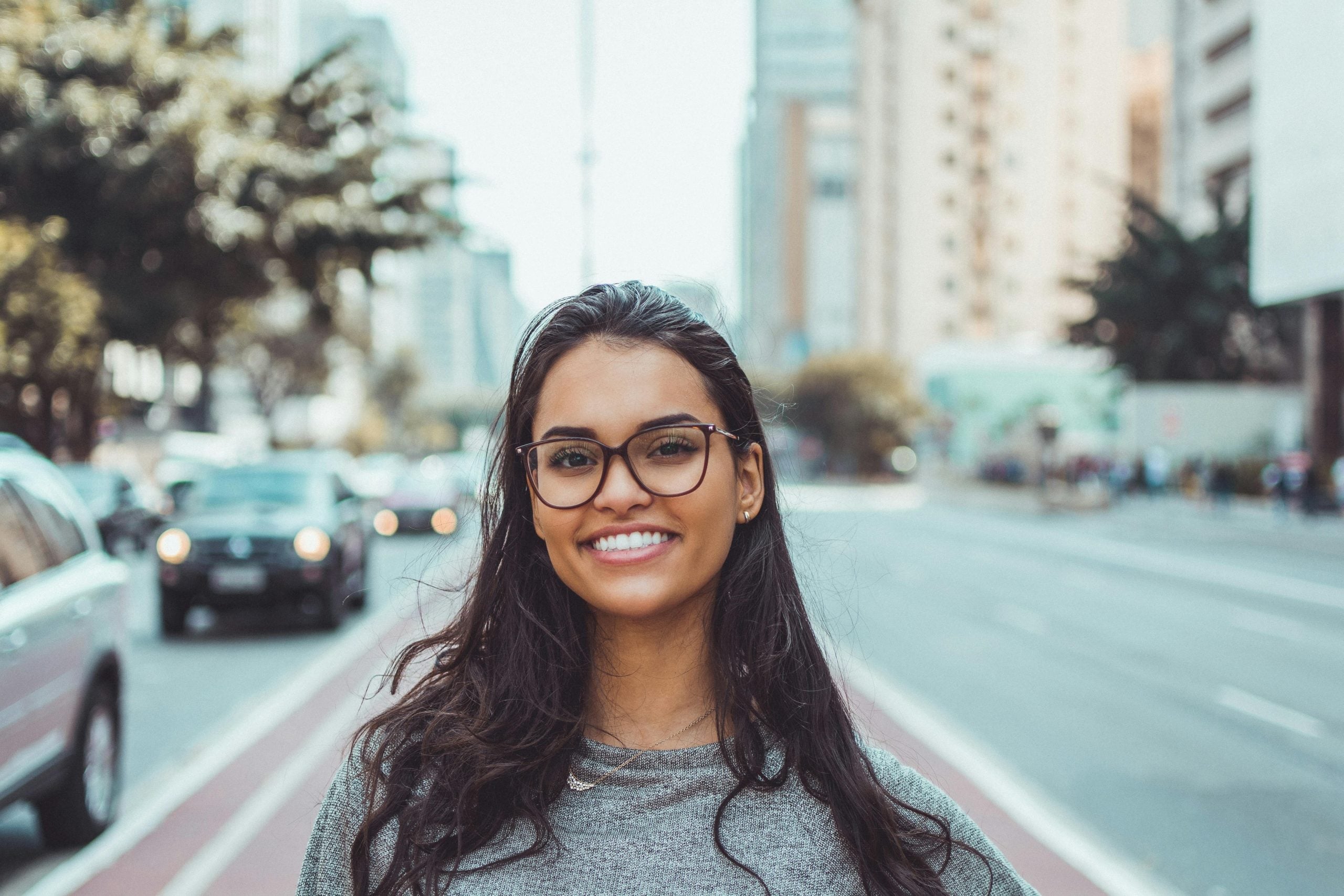 Young woman with glasses smiling confidently on urban city street
