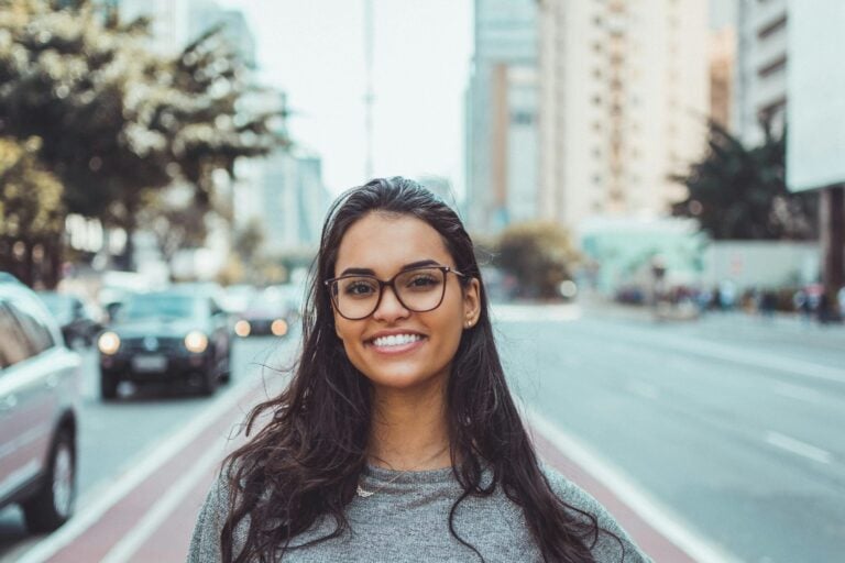 Young woman with glasses smiling confidently on urban city street