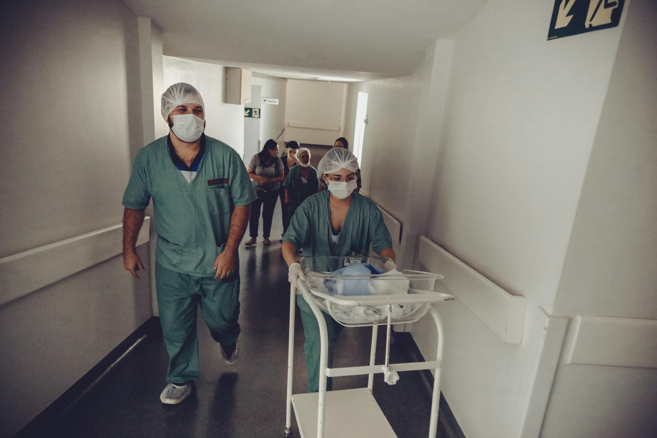 Healthcare team in surgical attire transporting newborn through hospital corridor