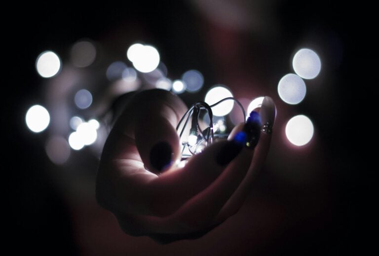 Hand holding glowing lightbulb surrounded by bokeh lights in darkness