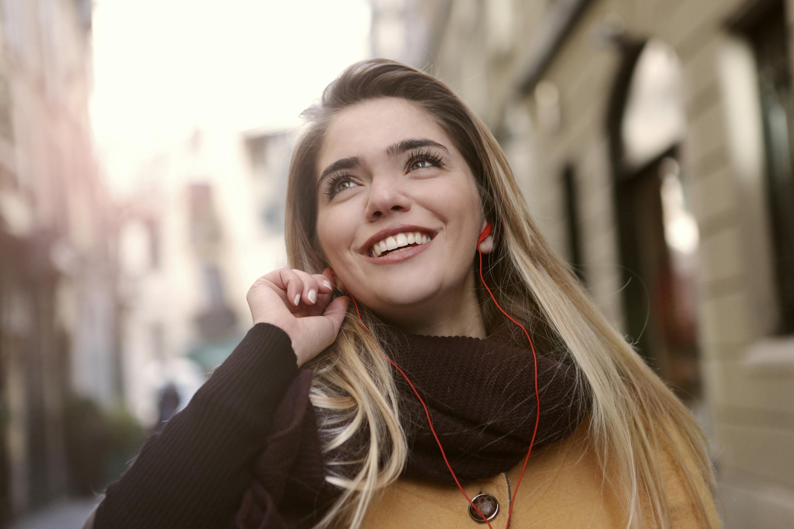 Joyful young woman enjoying music with earphones on bright day in the city.