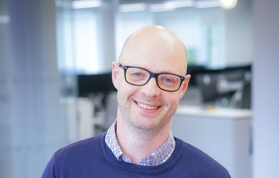 Smiling bald man with glasses in modern office workspace portrait