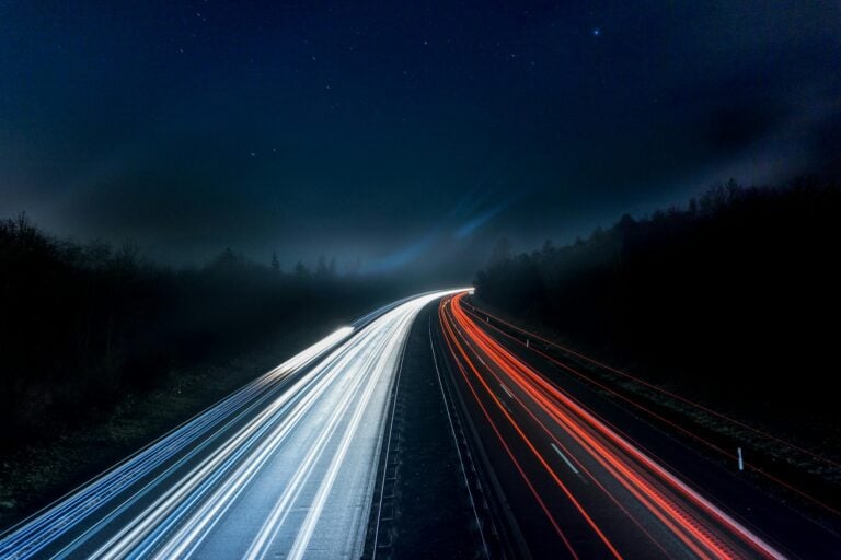 Long exposure night photograph capturing red and white light trails on highway.
