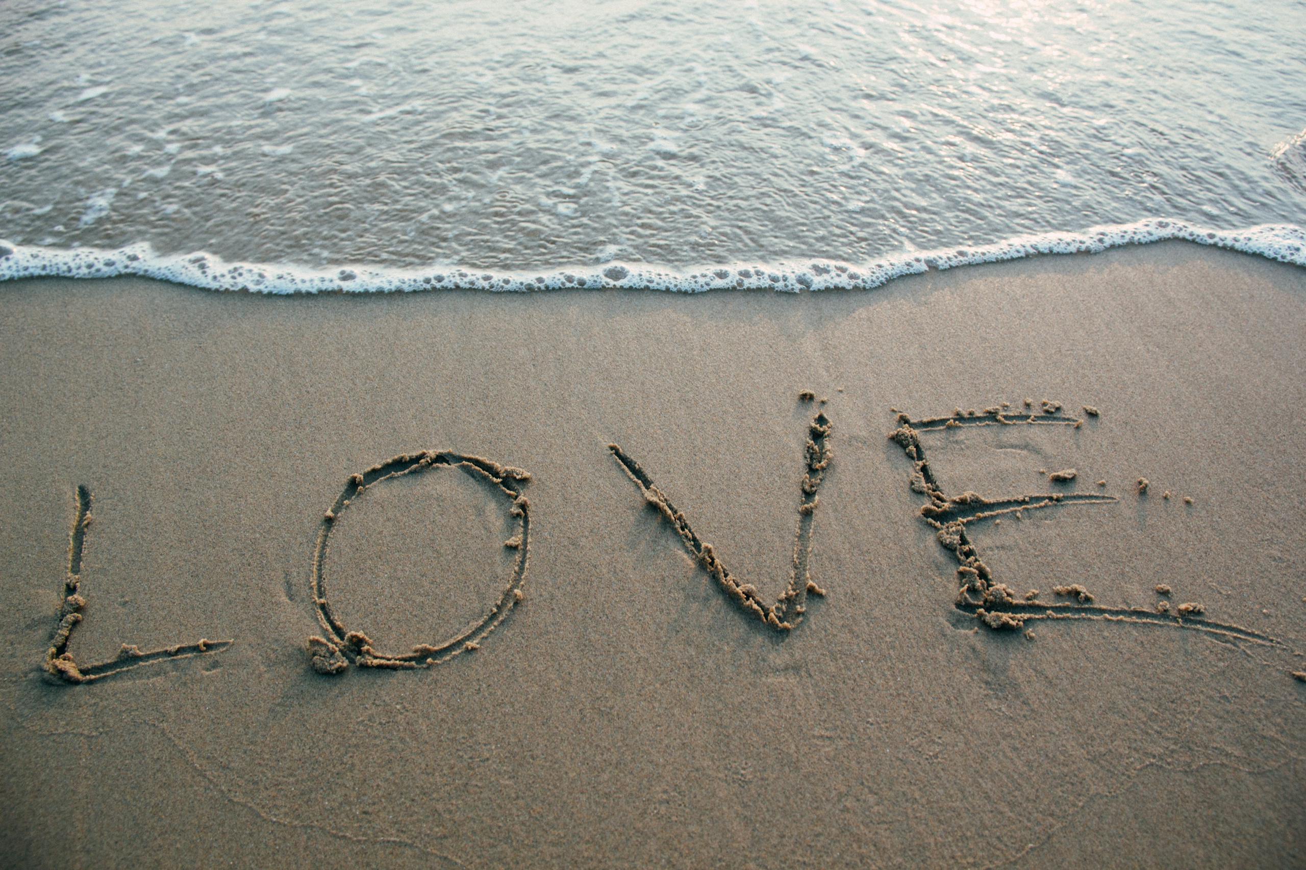 Love written in sand with ocean waves at beach evoking romance and tranquility
