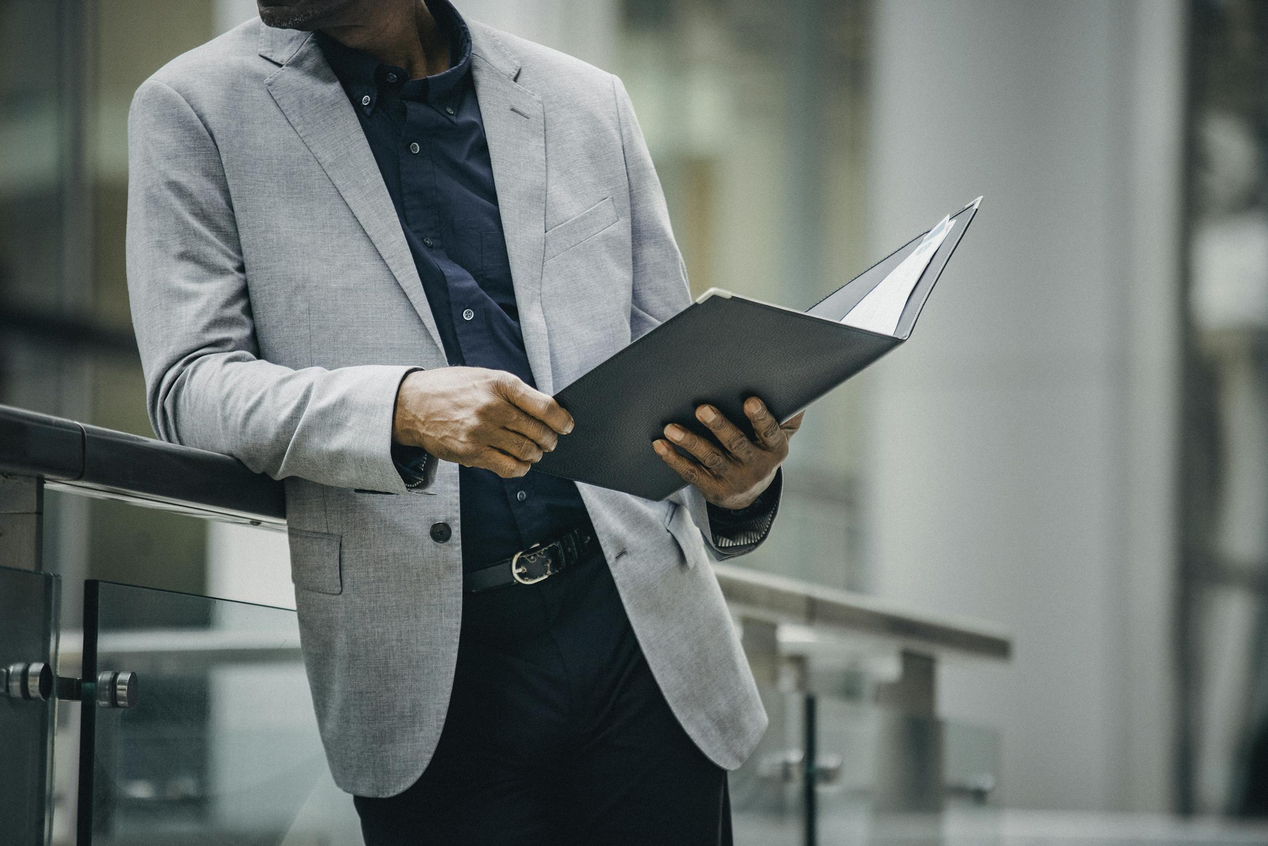 Man in suit reviews documents leaning on railing outdoors, professional and focused.