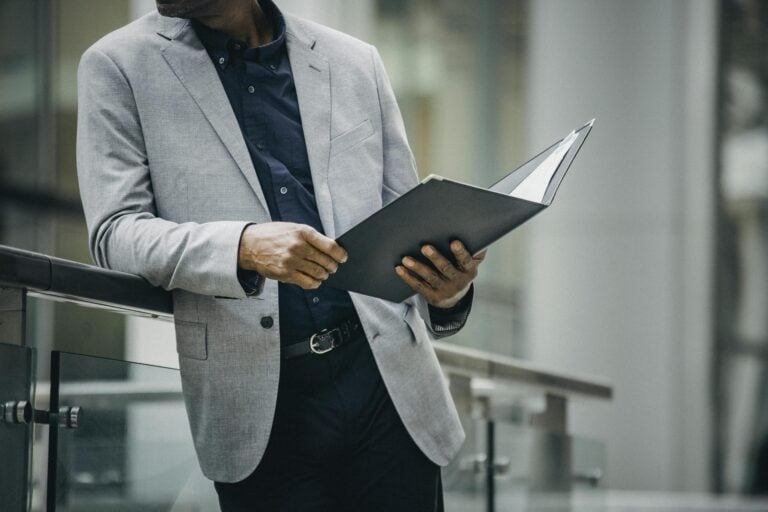 Man in suit reviews documents leaning on railing outdoors, professional and focused.